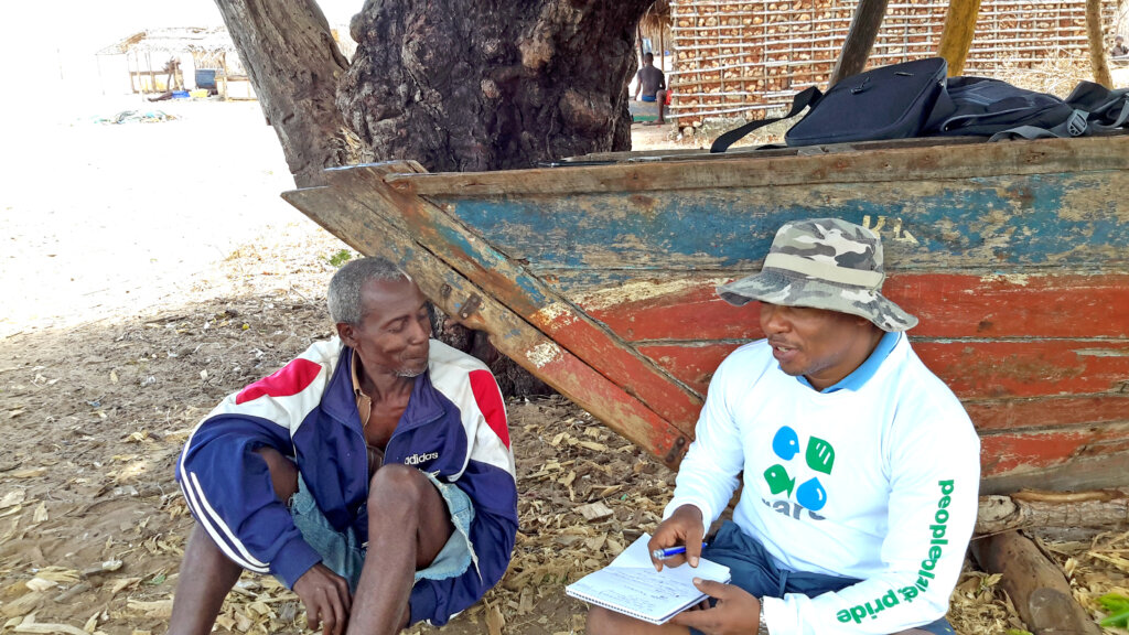 A fisher speaks with a Rare staff member in front of a boat